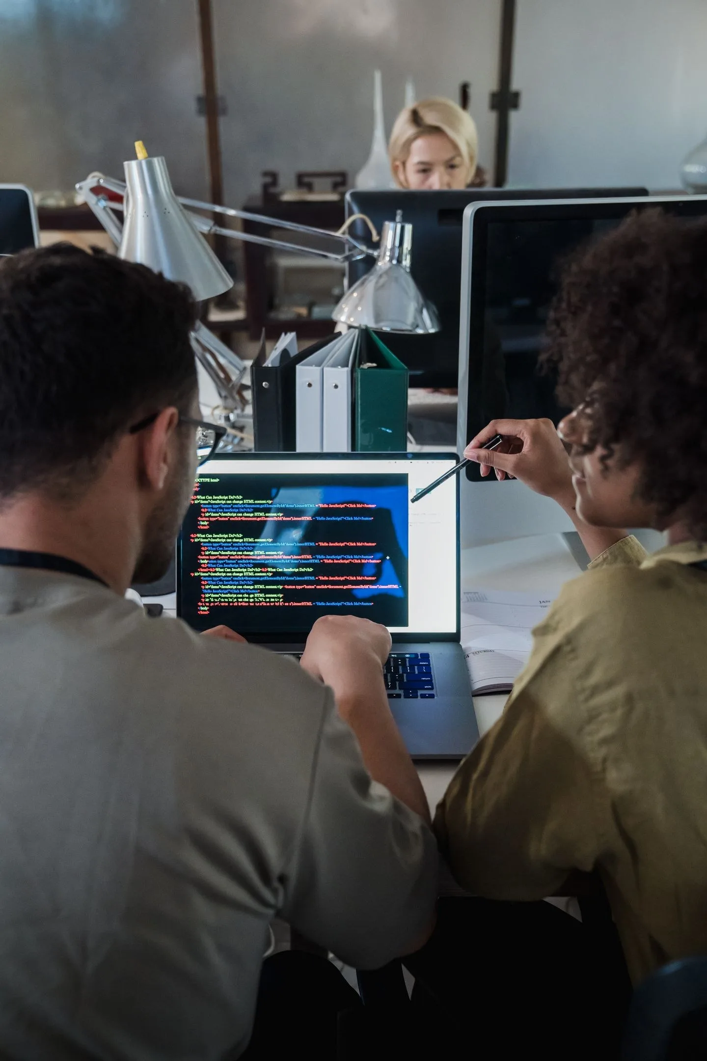 Two developers engage in software programming on a laptop in a modern office setting.
