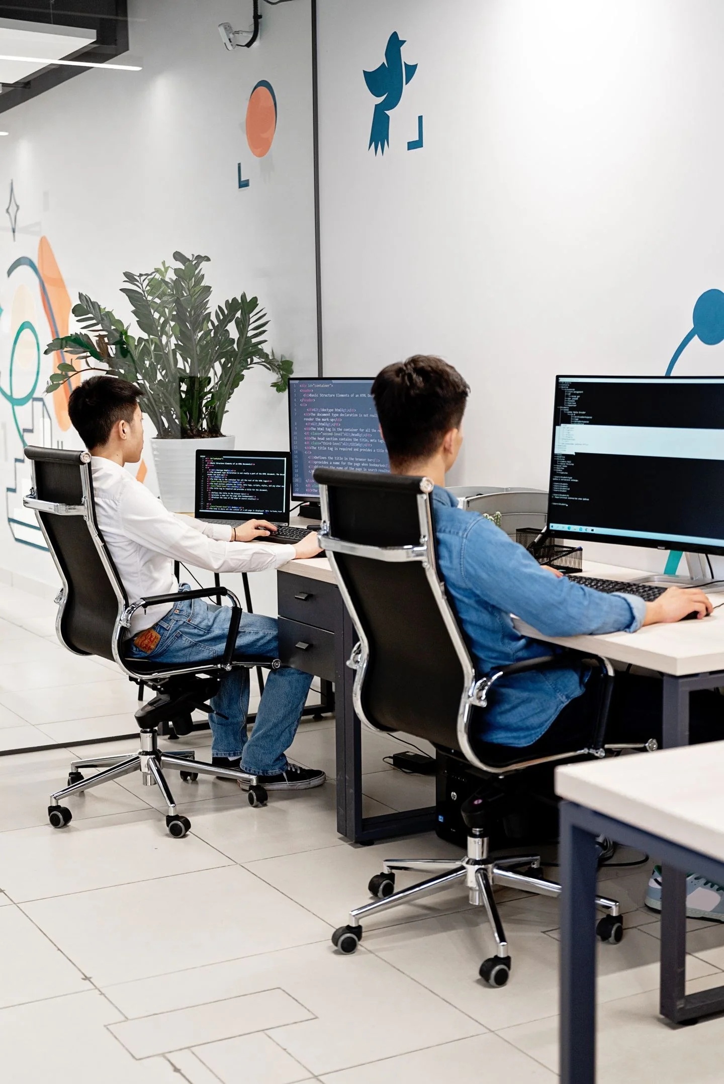 Two programmers collaborating in a bright, modern office, coding on monitors.