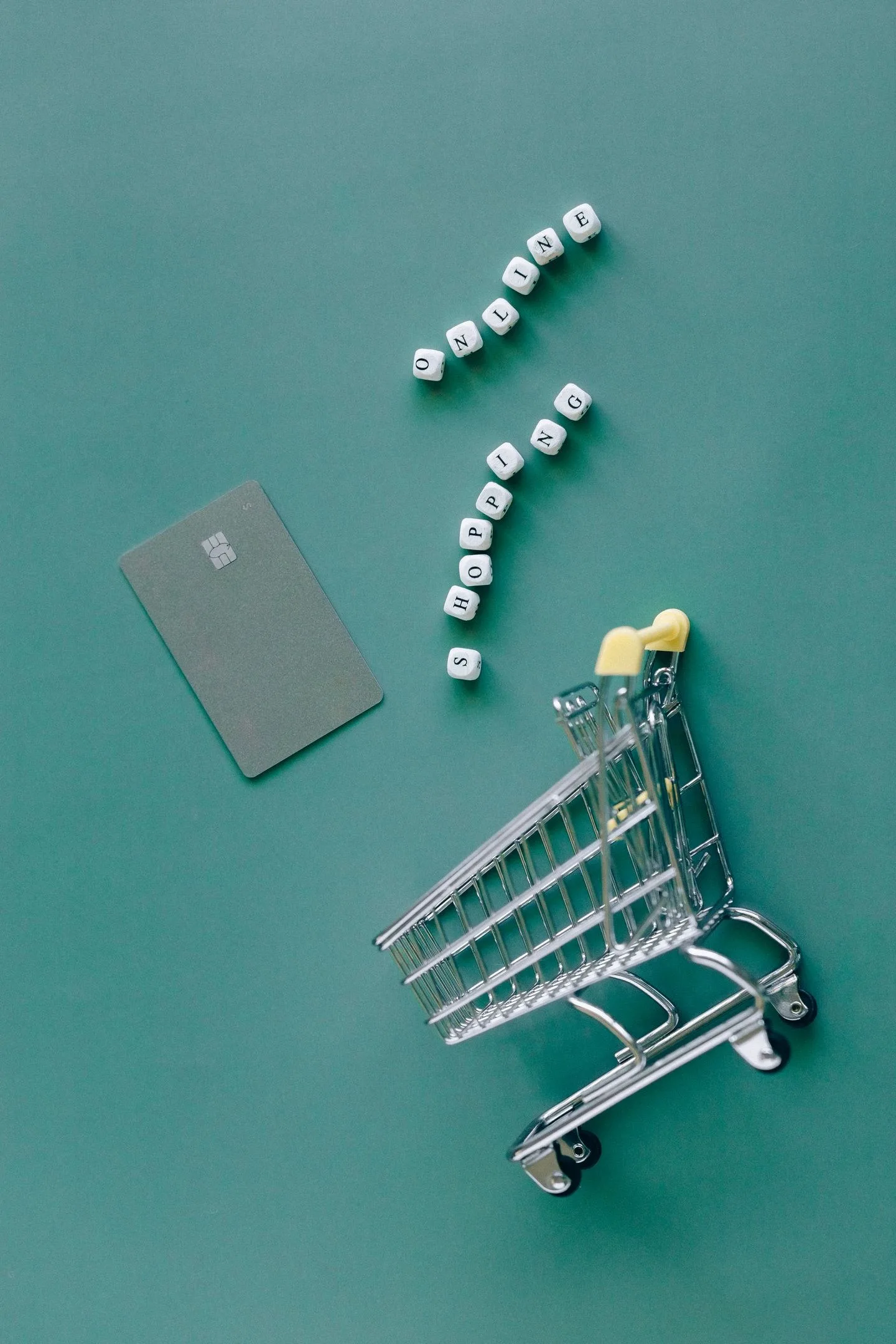 A conceptual image featuring a mini shopping cart, credit card, and letter blocks spelling 'online shopping' on a green background.