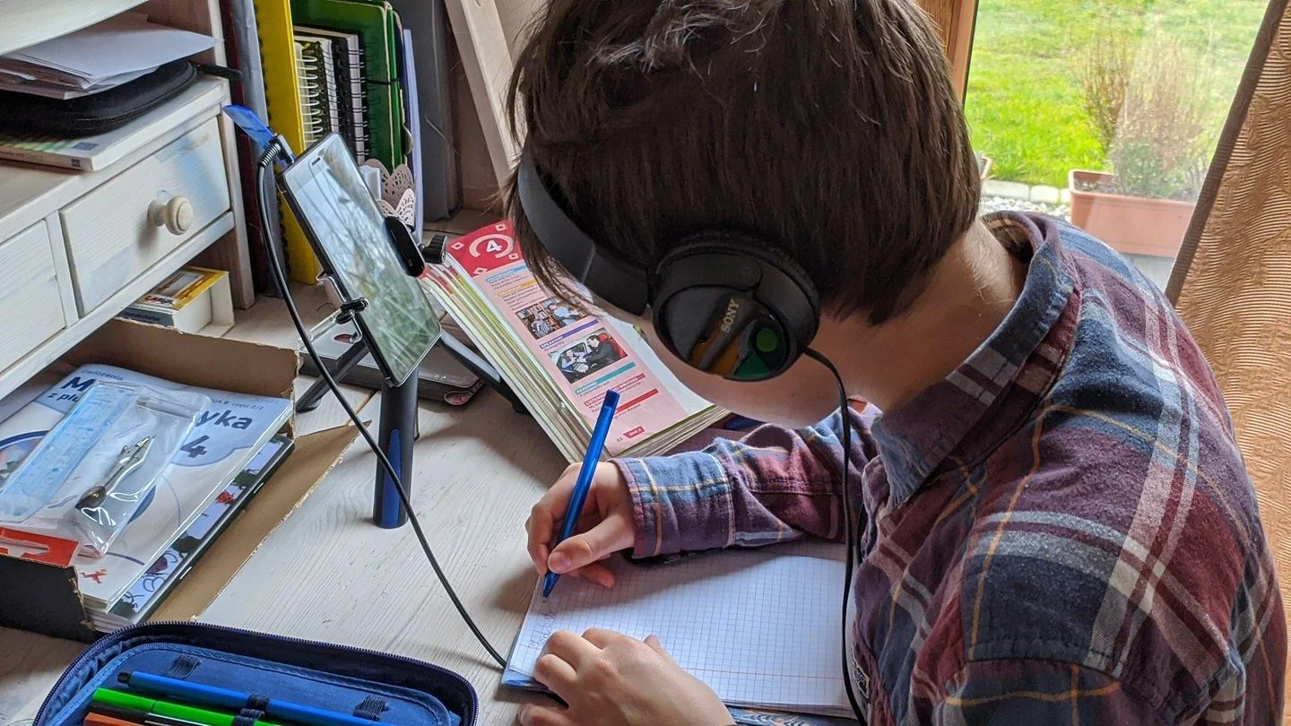 Young boy writing notes during an online class at home, focused on studying.