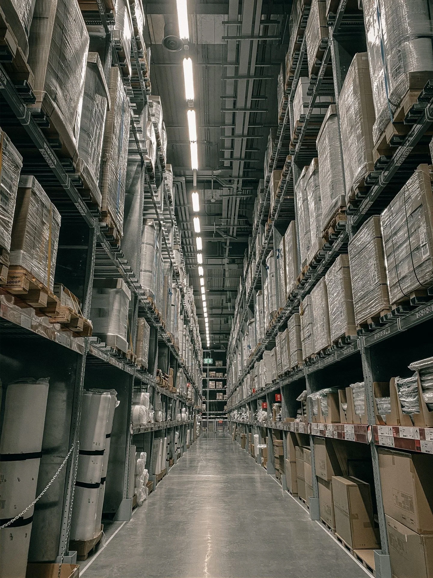 A long aisle in a modern warehouse with high shelving filled with boxes and supplies.