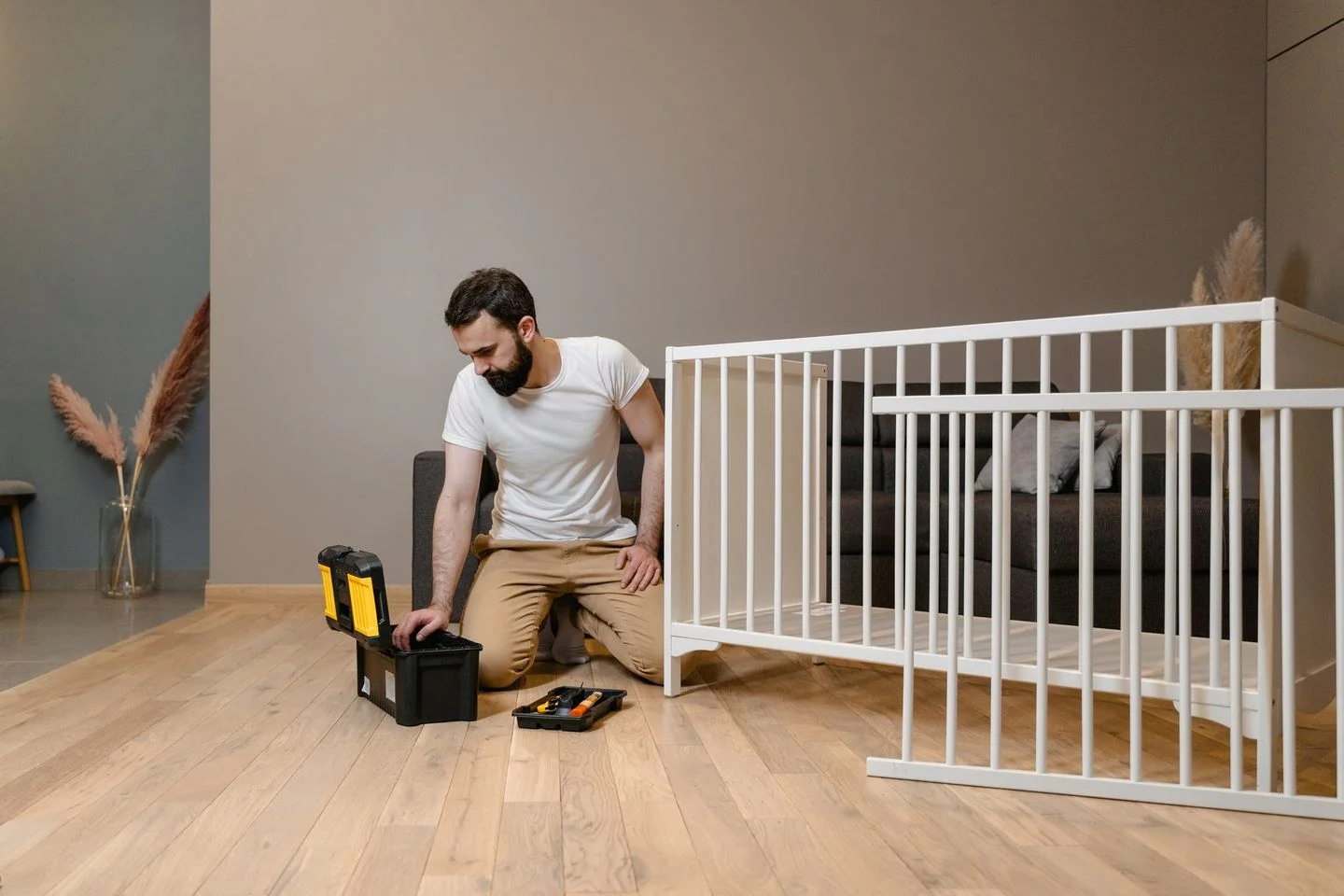 A man assembling a white crib indoors with tools, focusing on DIY and home care.