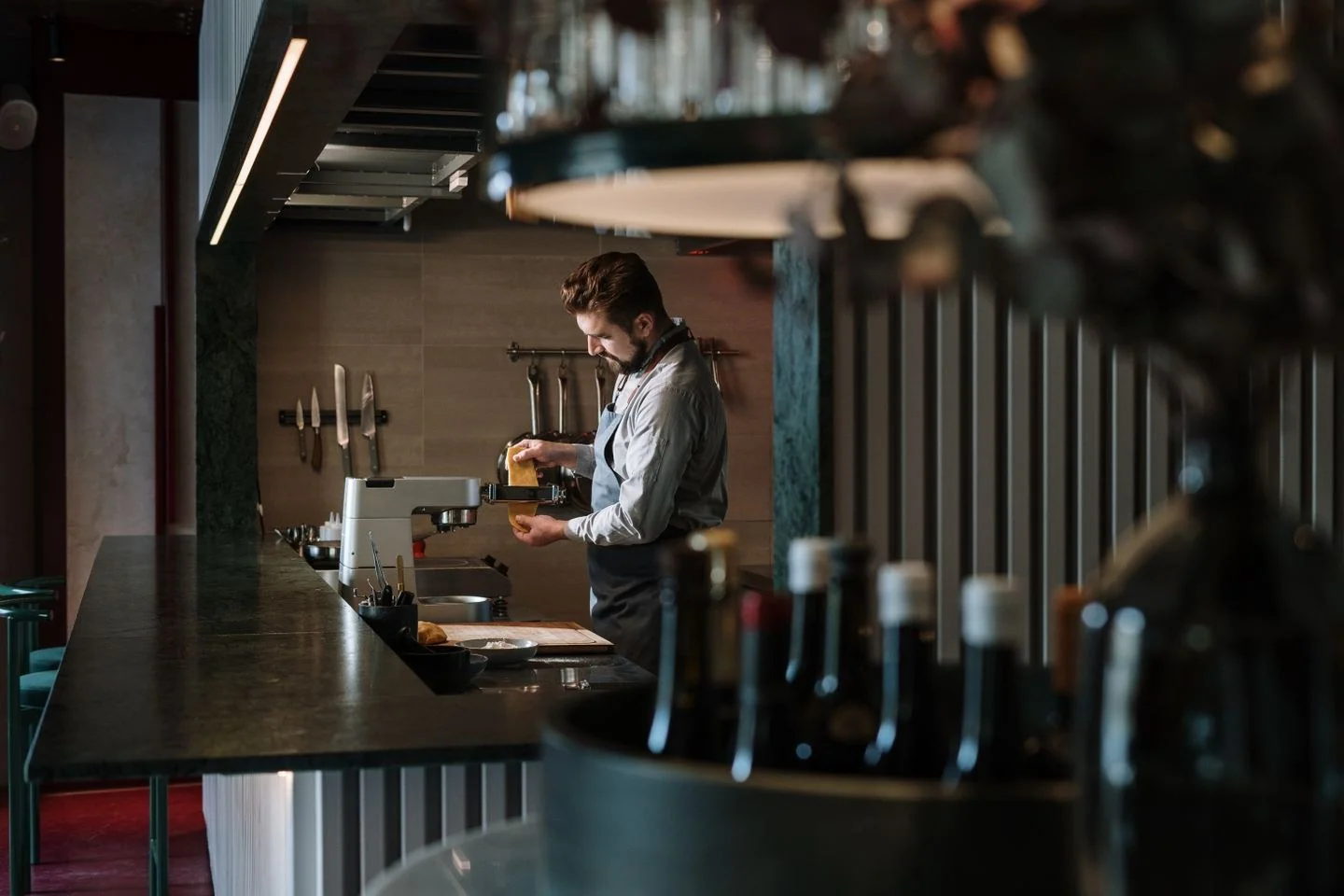 A male chef meticulously prepares a dish in a contemporary restaurant kitchen, surrounded by culinary tools.