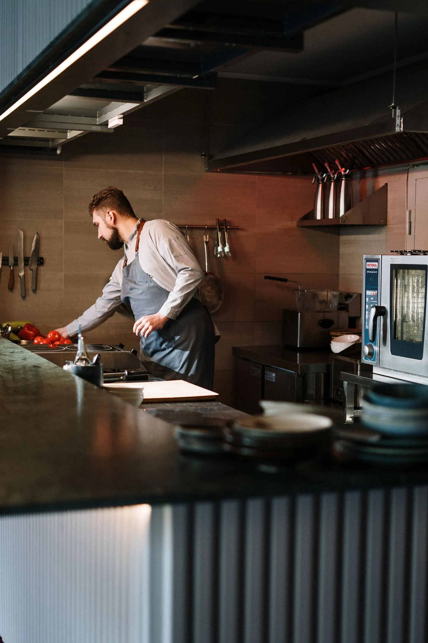 Chef in apron preparing food in a modern kitchen with stainless steel equipment.