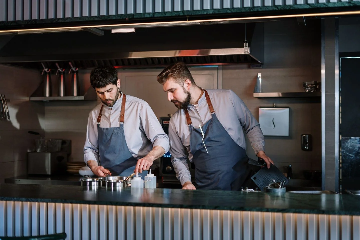 Two male chefs in aprons cook attentively in a contemporary open kitchen setting.