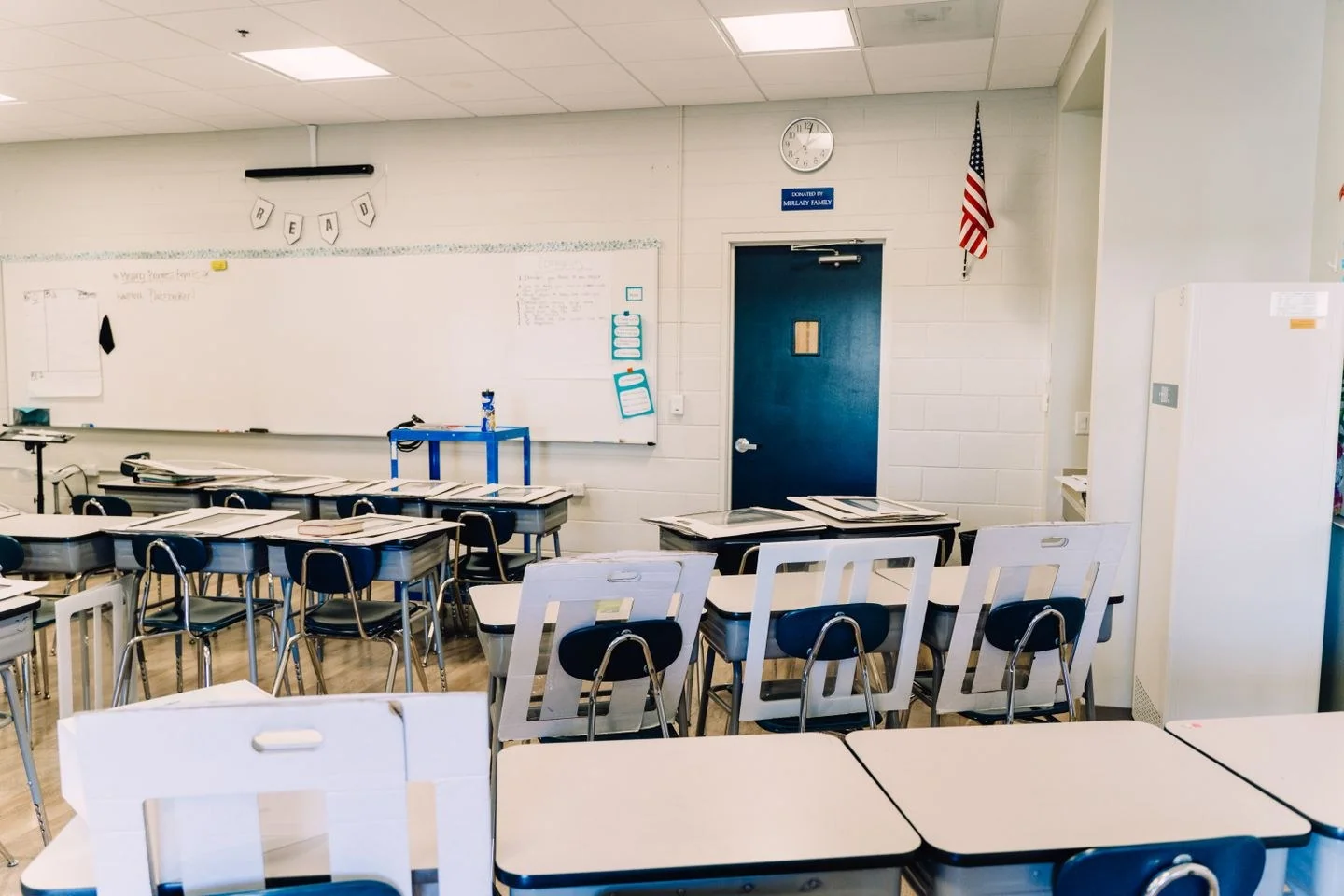 Bright empty classroom featuring desks, a whiteboard, and an American flag. Ideal learning environment.
