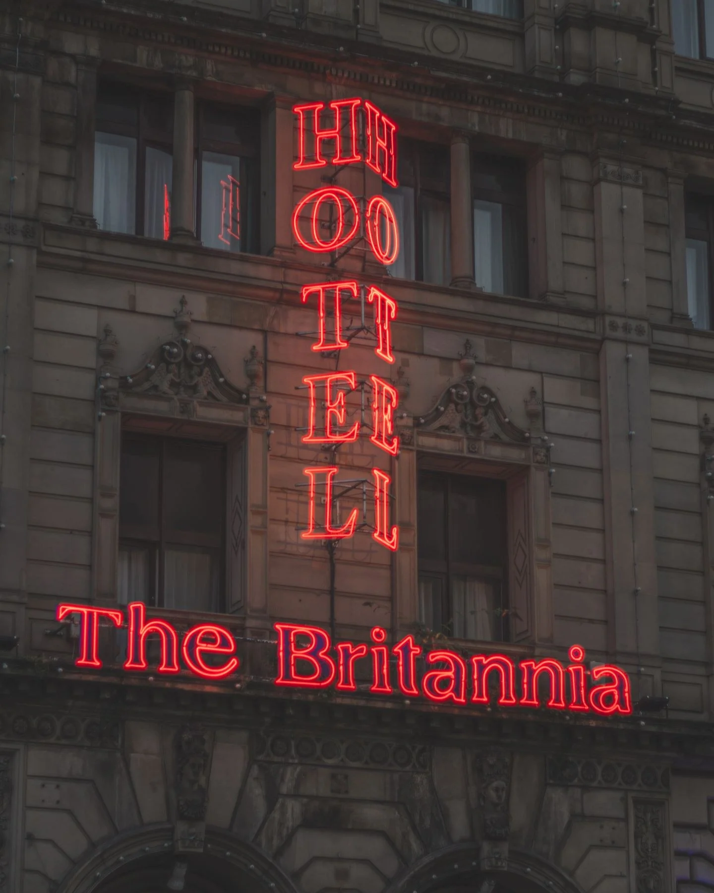 Neon lights of Britannia Hotel sign glowing against historic facade at night in Manchester.